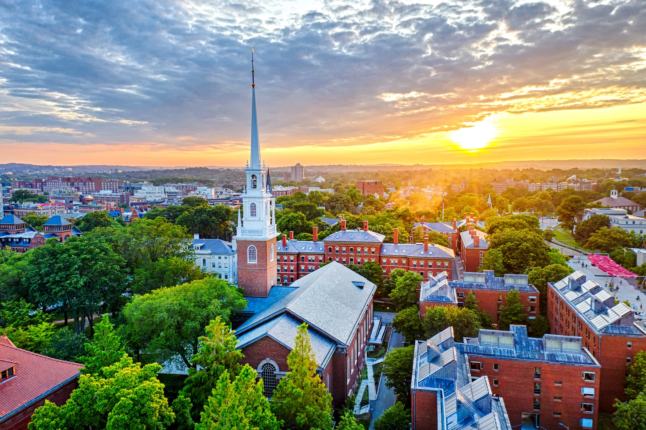 Aerial view of a college campus at sunset, featuring a prominent church steeple and tree-filled surroundings, reflecting a serene academic atmosphere.
