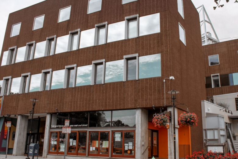 Modern building with a brown exterior featuring large windows. The entrance is adorned with flower baskets, adding charm and inviting ambiance.