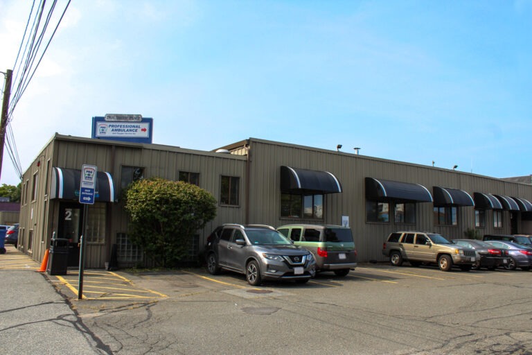 Professional Ambulance building with a sign visible. Several vehicles parked in front and a landscaped area add to the overall setting.