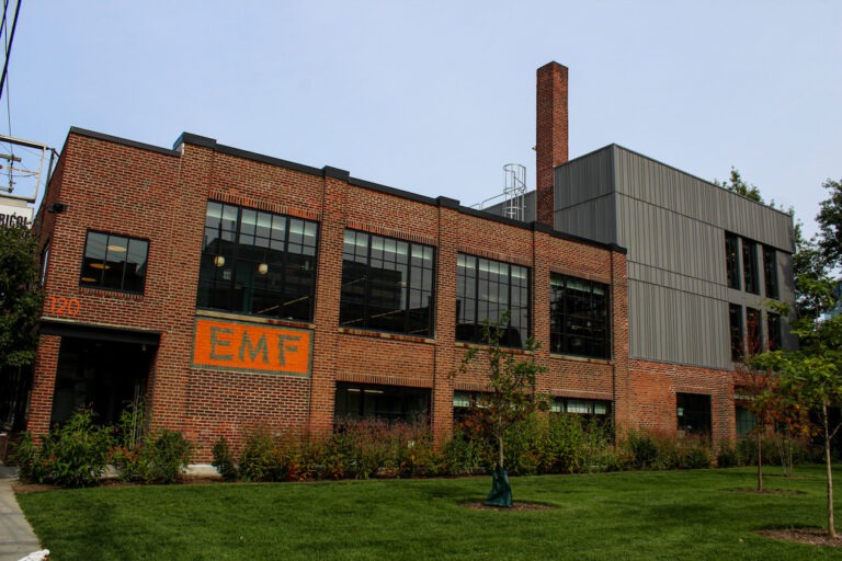 Brick building labeled "EMF" with modern additions, surrounded by greenery, showcasing a blend of industrial and contemporary architecture.