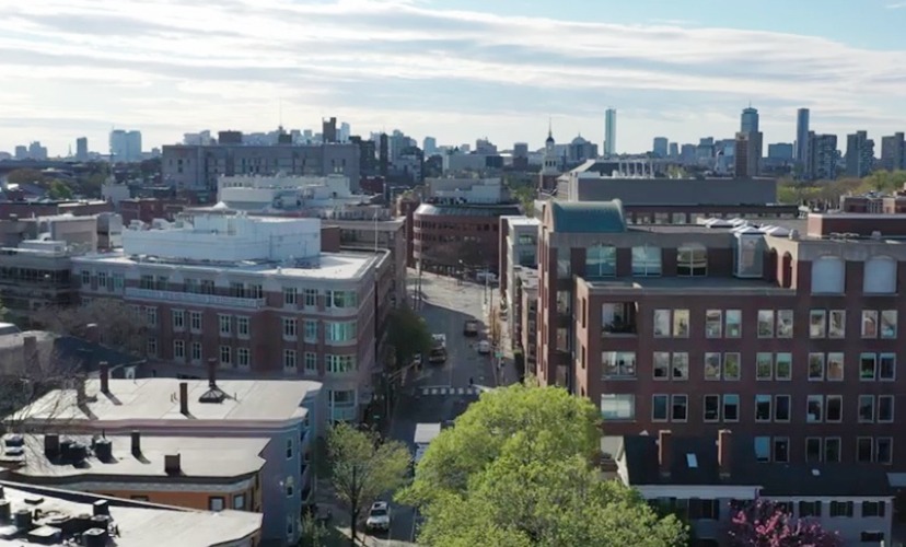 Aerial view of a cityscape featuring a mix of historic and modern buildings, with a clear skyline in the background on a sunny day.